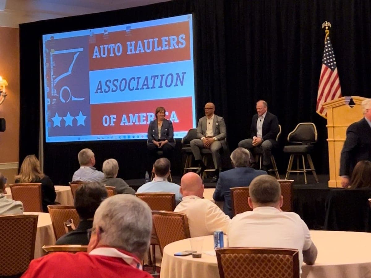 A panel discussion on stage at the Auto Haulers Association of America conference, with the association's logo on the screen.