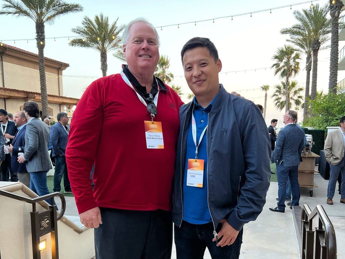 Two attendees of the Finished Vehicle Logistics conference standing on an outdoor terrace lined with palm trees.